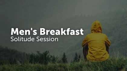 Man in a yellow rain jacket sitting alone on a grassy hillside overlooking a misty forest, with the text Men's Breakfast, Solitude Session